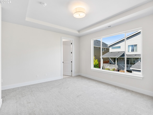empty room featuring carpet, a tray ceiling, baseboards, and visible vents