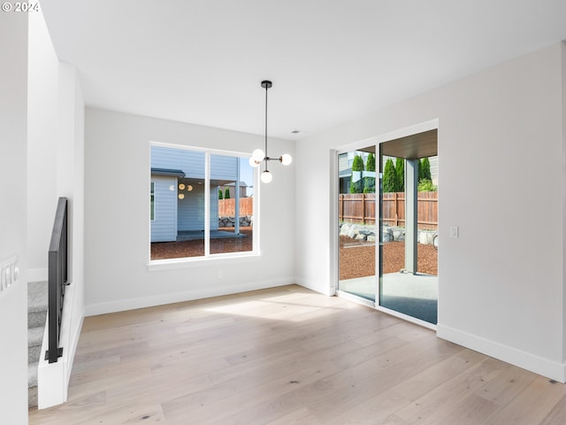unfurnished dining area with baseboards, light wood-style flooring, and an inviting chandelier
