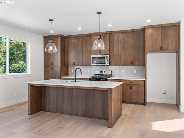 kitchen featuring light countertops, tasteful backsplash, a sink, light wood finished floors, and appliances with stainless steel finishes