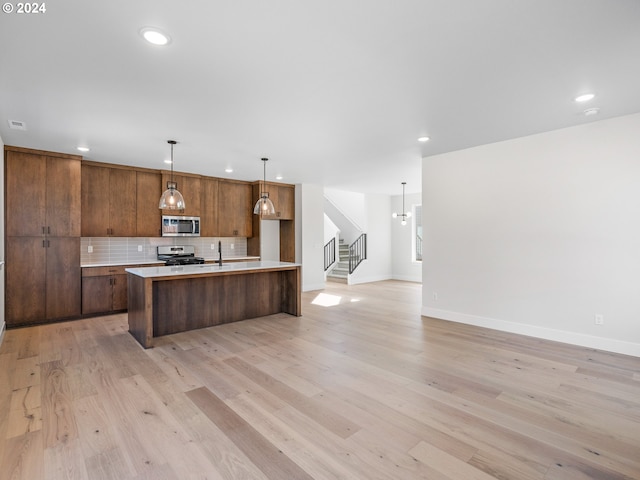 kitchen with open floor plan, light countertops, backsplash, light wood finished floors, and appliances with stainless steel finishes
