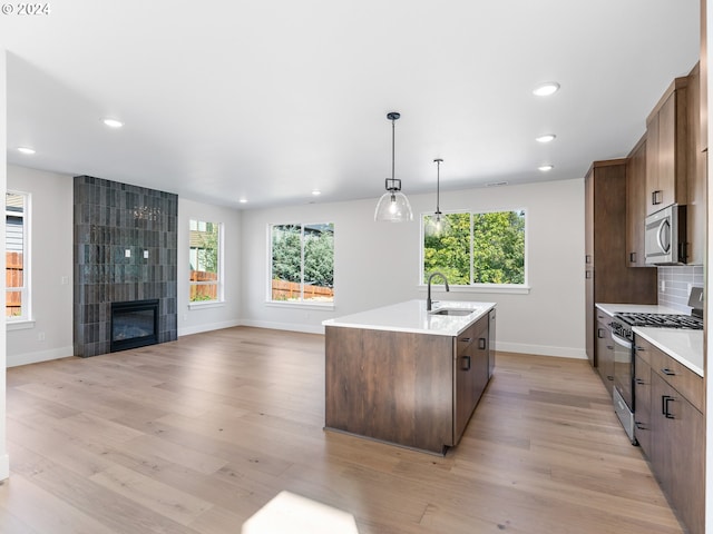 kitchen with backsplash, a center island with sink, stainless steel appliances, and light wood-style floors