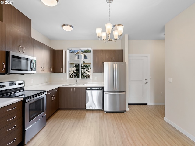 kitchen featuring appliances with stainless steel finishes, sink, decorative light fixtures, light hardwood / wood-style flooring, and a notable chandelier