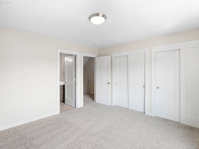 unfurnished bedroom featuring light carpet, ensuite bath, and multiple closets