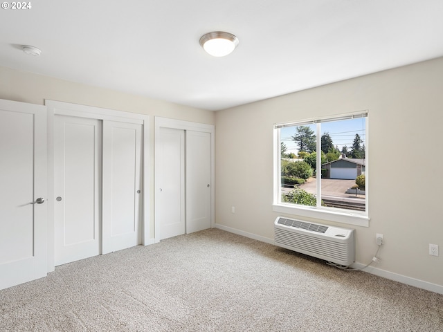 unfurnished bedroom featuring carpet floors, an AC wall unit, and two closets