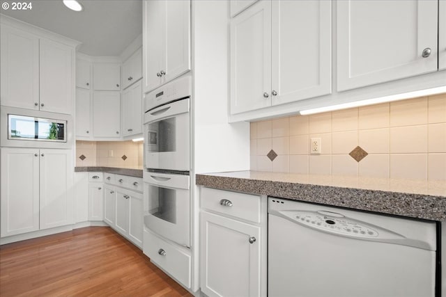 kitchen with light hardwood / wood-style floors, backsplash, white appliances, light stone countertops, and white cabinets