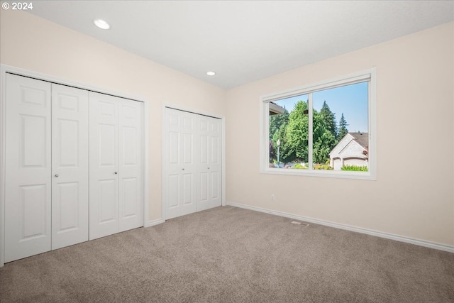 unfurnished bedroom featuring carpet floors and two closets