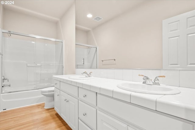 full bathroom featuring toilet, vanity, backsplash, hardwood / wood-style floors, and shower / bath combination with glass door