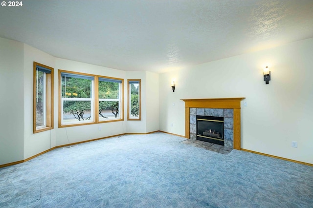 unfurnished living room with carpet floors, visible vents, a textured ceiling, a tile fireplace, and baseboards