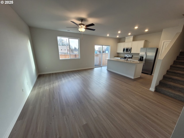 kitchen with a center island with sink, baseboards, appliances with stainless steel finishes, open floor plan, and white cabinetry