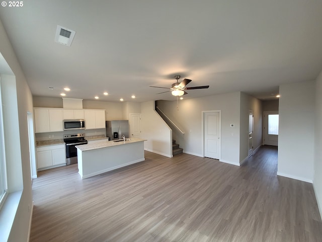 kitchen with a kitchen island with sink, stainless steel appliances, white cabinetry, visible vents, and light wood-style floors