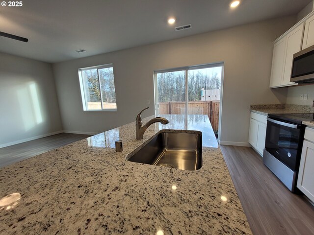 kitchen with light stone counters, range with electric stovetop, stainless steel microwave, visible vents, and a sink