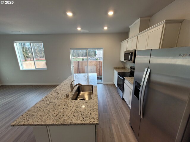 kitchen with white cabinets, plenty of natural light, a kitchen island with sink, and stainless steel appliances