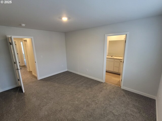 unfurnished bedroom featuring connected bathroom, baseboards, dark colored carpet, and a sink