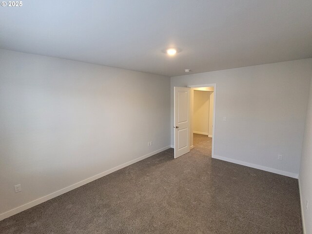 spare room with dark carpet and baseboards