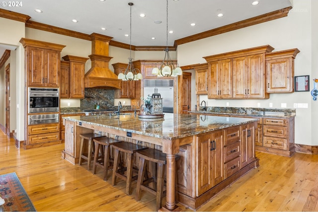 kitchen featuring a spacious island, appliances with stainless steel finishes, a breakfast bar, dark stone countertops, and light hardwood / wood-style flooring