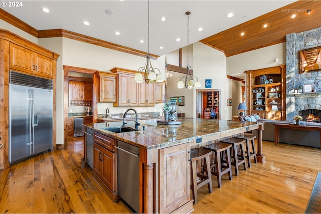 kitchen featuring a center island with sink, sink, appliances with stainless steel finishes, dark stone counters, and light wood-type flooring