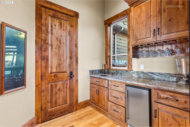 kitchen with light hardwood / wood-style floors, dark stone counters, sink, and stainless steel refrigerator