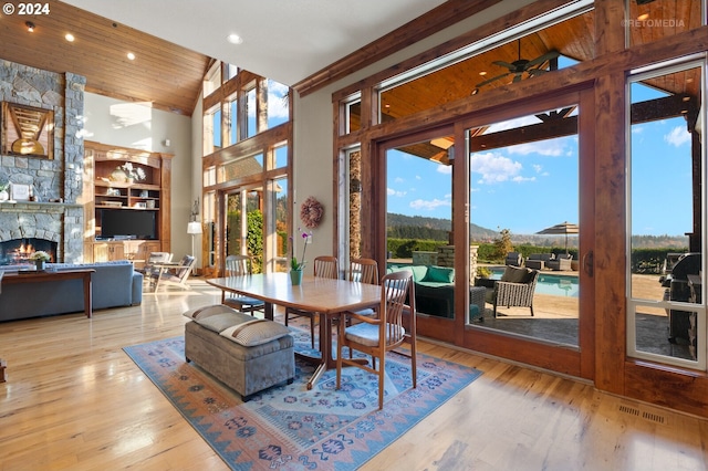 dining area with light wood-type flooring, a fireplace, ceiling fan, and high vaulted ceiling