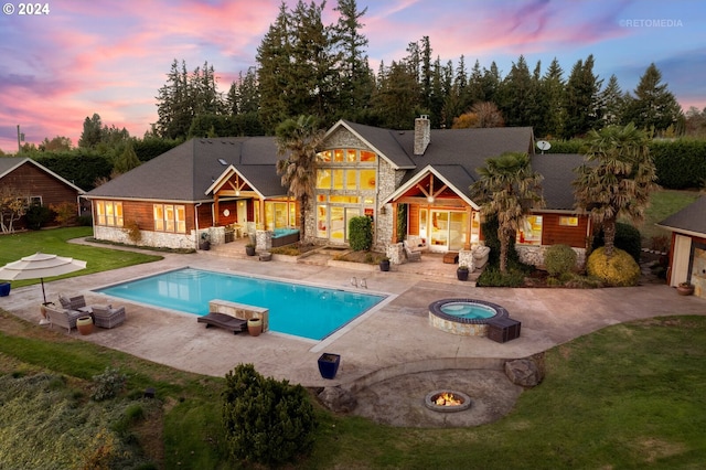 pool at dusk with a patio area, a lawn, an outdoor fire pit, and an in ground hot tub