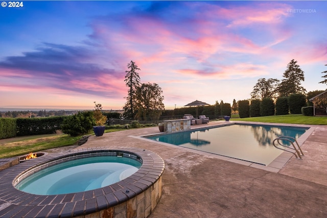 pool at dusk featuring an in ground hot tub and a patio area