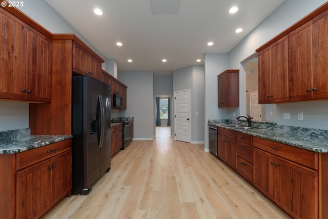 kitchen with dark stone countertops, a barn door, dishwasher, light hardwood / wood-style flooring, and sink