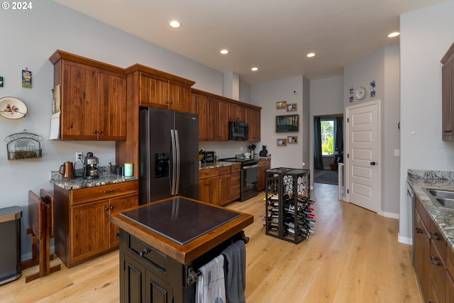 kitchen with light wood-type flooring, sink, a kitchen island, black appliances, and stone countertops