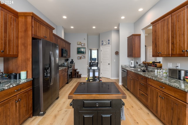 kitchen featuring light hardwood / wood-style floors, sink, a kitchen island, stainless steel appliances, and dark stone countertops