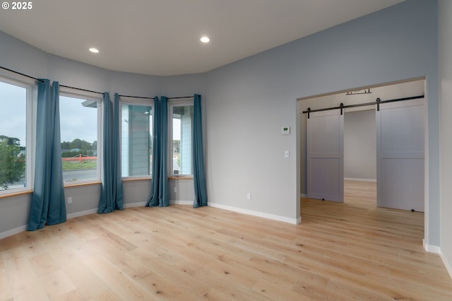 unfurnished room featuring light wood finished floors, a barn door, baseboards, and recessed lighting