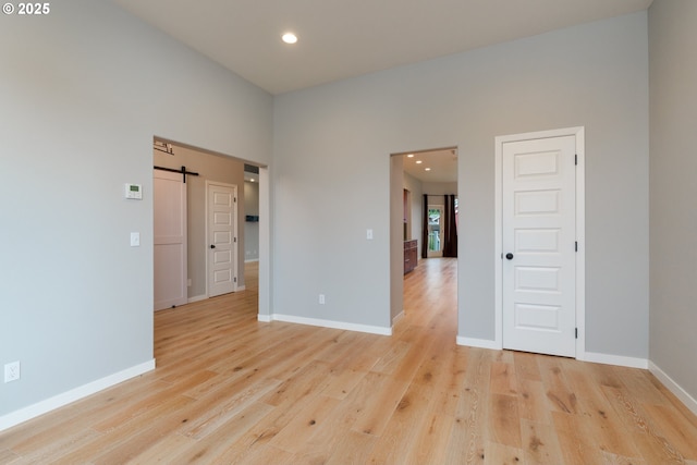 unfurnished room featuring a barn door, recessed lighting, light wood-style flooring, and baseboards