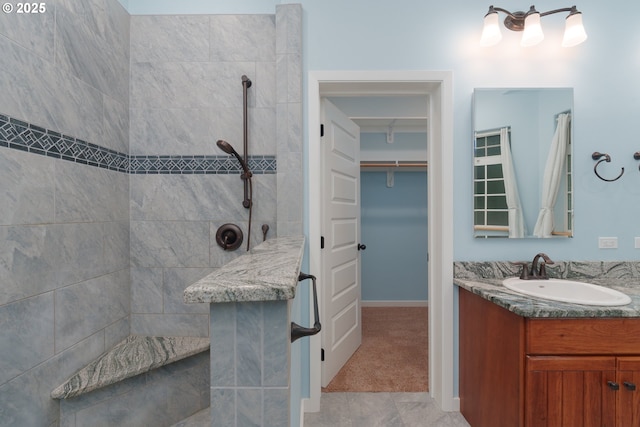 bathroom featuring a walk in closet, vanity, baseboards, and a walk in shower