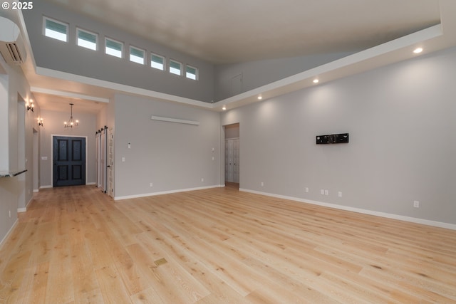 spare room featuring high vaulted ceiling, a wall unit AC, light wood-style flooring, baseboards, and an inviting chandelier