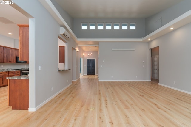 living area featuring baseboards, a wall mounted AC, a towering ceiling, and light wood-style floors