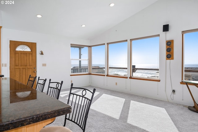 dining area featuring light carpet, lofted ceiling, and a water view