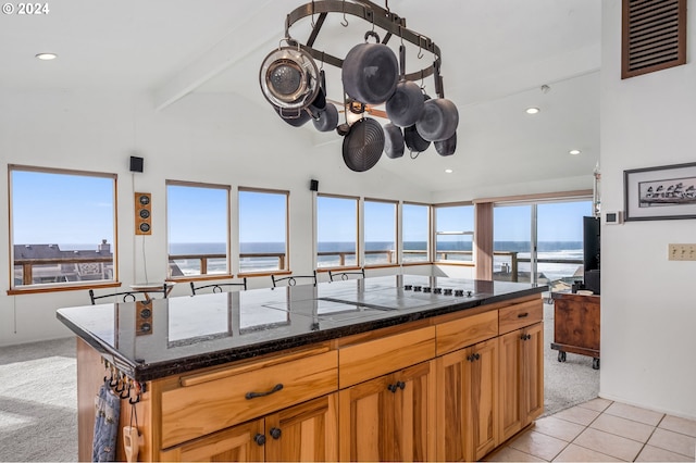 kitchen with lofted ceiling with beams, light colored carpet, a kitchen island, a water view, and black electric cooktop