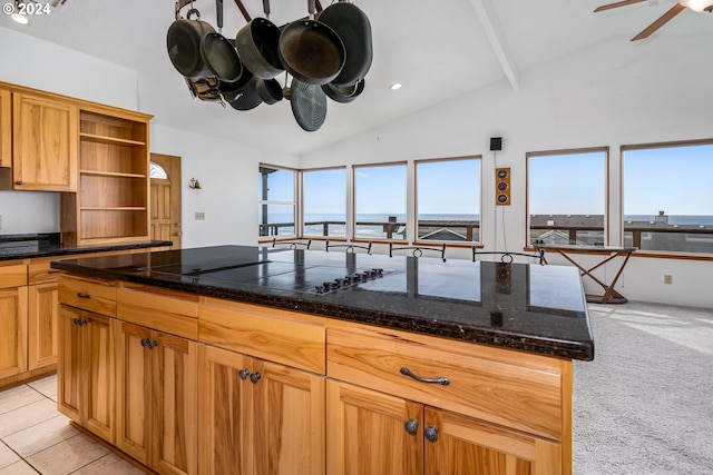 kitchen featuring ceiling fan, lofted ceiling, dark stone countertops, light carpet, and a water view