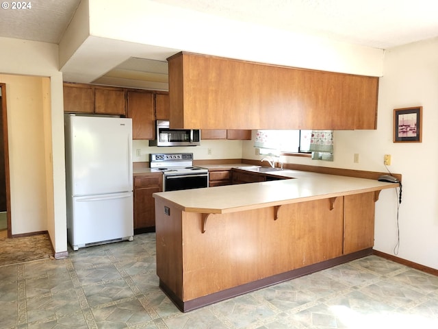 kitchen featuring a breakfast bar area, white appliances, sink, and kitchen peninsula