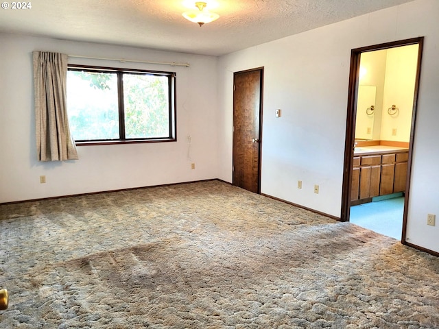 unfurnished bedroom with a textured ceiling, carpet flooring, and ensuite bathroom