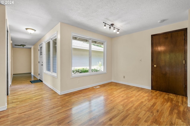 empty room featuring light hardwood / wood-style floors, a textured ceiling, and track lighting