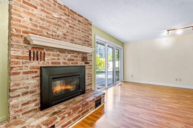 unfurnished living room featuring a textured ceiling, brick wall, a brick fireplace, and light wood-type flooring