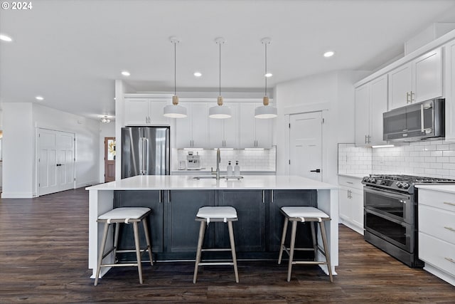 kitchen featuring dark wood-type flooring, decorative light fixtures, stainless steel appliances, and a center island with sink