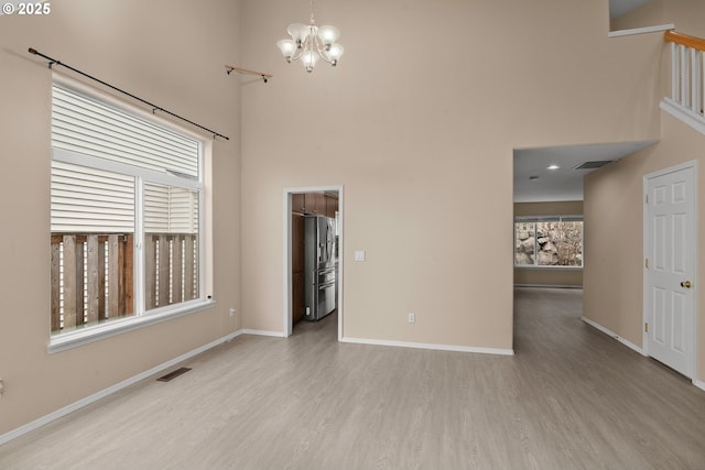 unfurnished room featuring a towering ceiling, light wood-type flooring, and an inviting chandelier