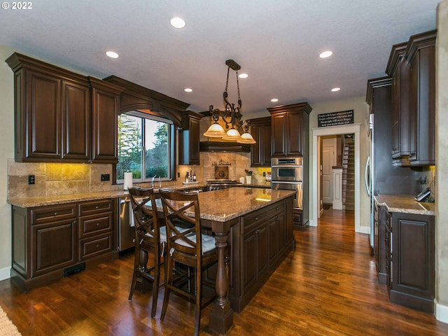 kitchen with decorative light fixtures, dark wood-type flooring, tasteful backsplash, a kitchen island, and stainless steel appliances