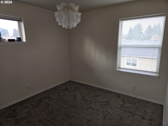 unfurnished room with dark colored carpet and a chandelier