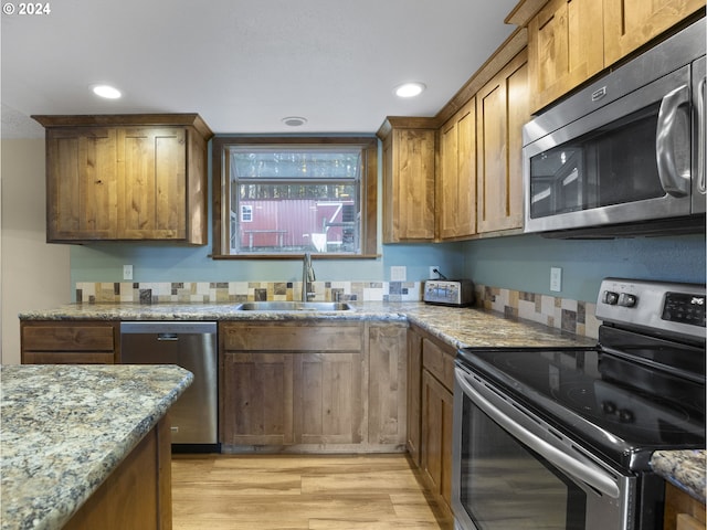 kitchen with light wood-type flooring, stainless steel appliances, light stone counters, and sink