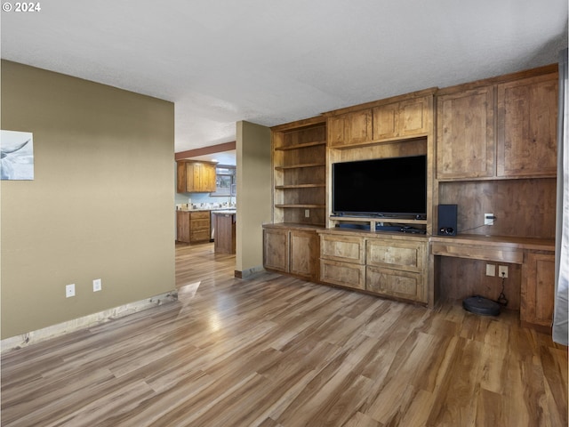 unfurnished living room featuring built in desk, a textured ceiling, and light hardwood / wood-style flooring