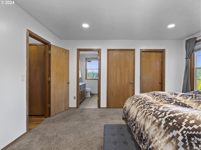 bedroom with two closets, light colored carpet, connected bathroom, and multiple windows