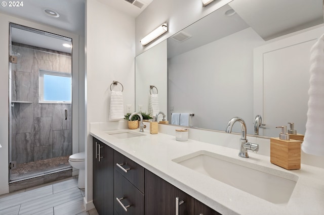 bathroom with dual vanity, tiled shower, tile patterned flooring, and toilet