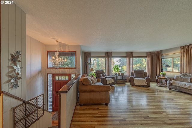 living room with a chandelier, wooden walls, wood-type flooring, and a textured ceiling