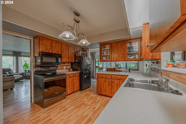 kitchen with pendant lighting, black appliances, sink, a notable chandelier, and light hardwood / wood-style floors