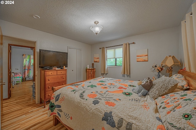 bedroom with a closet, a textured ceiling, and light wood-type flooring